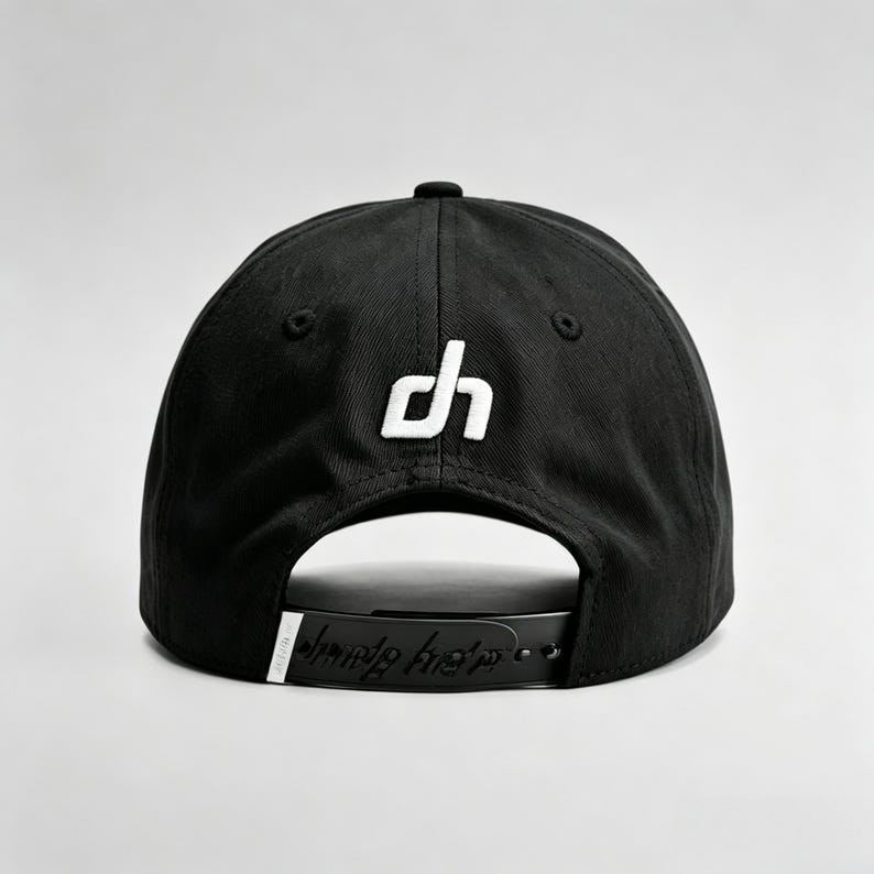 K&ouml;nnte beinhalten: Schwarze Baseballkappe mit wei&szlig;em "dh"-Logo auf der Vorderseite. Der verstellbare Riemen tr&auml;gt den Schriftzug "dune hats" in einer stilisierten Schriftart. Die Kappe ist aus strapazierf&auml;higem Stoff gefertigt und hat einen gebogenen Schirm.