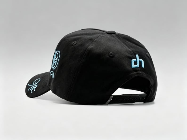 K&ouml;nnte beinhalten: Schwarze Baseballkappe mit flachem Schirm und verstellbarem Snapback-Verschluss. Die Kappe hat hellblaue gestickte Designs auf der Vorderseite, Seite und R&uuml;ckseite. Klassischer, sportlicher Stil.