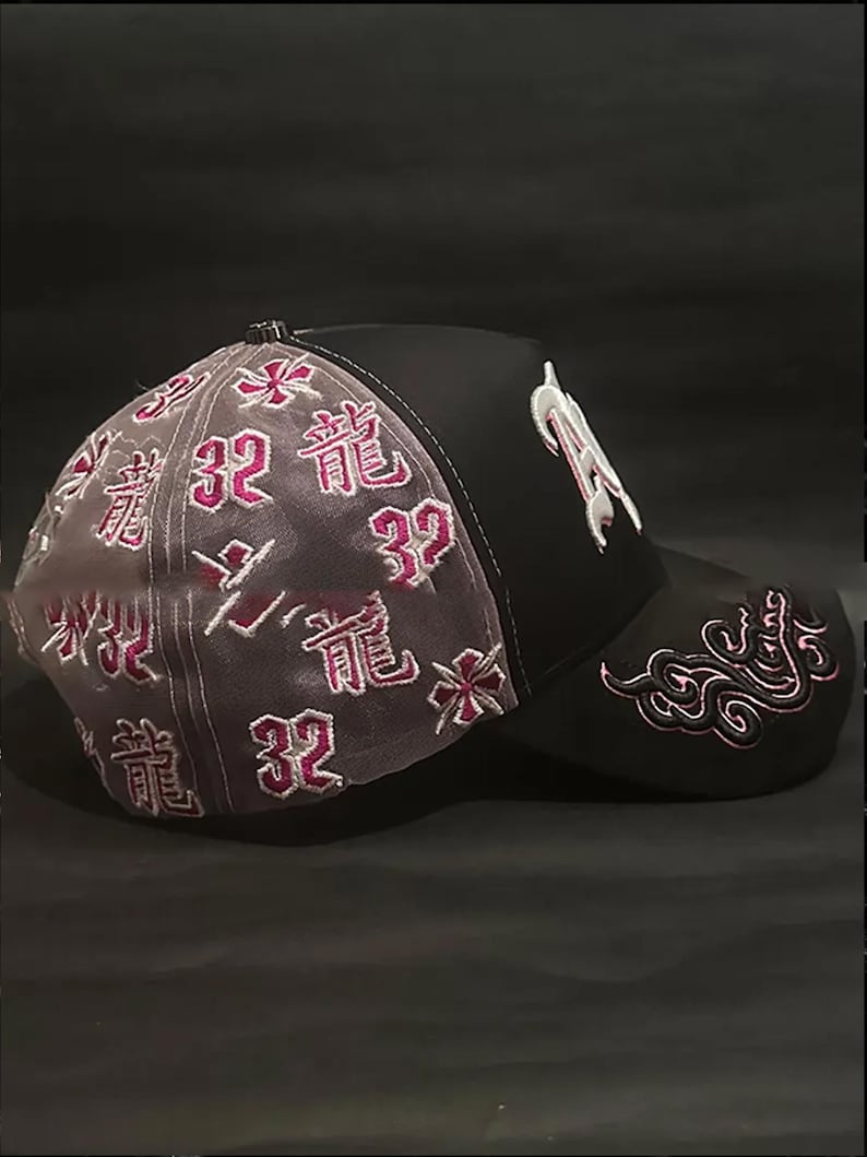 Peut inclure: Casquette de baseball noire avec des d&eacute;tails brod&eacute;s blancs et roses. La casquette pr&eacute;sente la lettre "R" en blanc sur le devant, et des textes et motifs floraux roses sur le c&ocirc;t&eacute; et &agrave; l'arri&egrave;re. Le panneau arri&egrave;re est en mat&eacute;riau gris transparent.