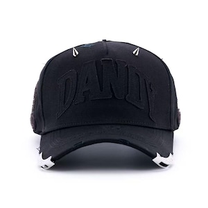 Puede incluir: Gorra de béisbol negra con la palabra "DANDY" cosida en la parte delantera. La gorra tiene púas plateadas y detalles desgastados en el borde. La gorra es de color oscuro y tiene una visera curva.