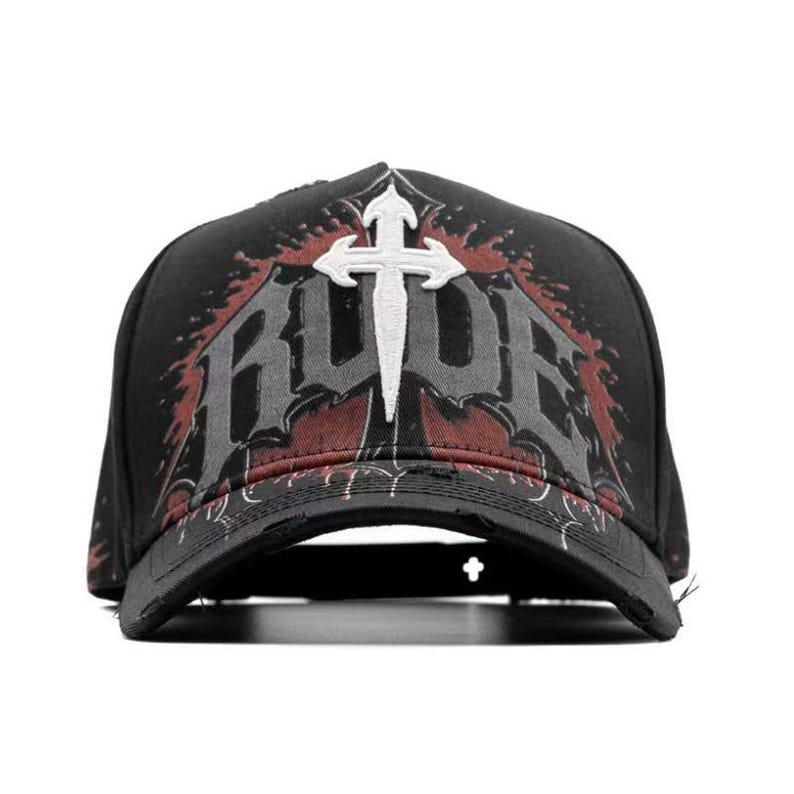 May include: Black baseball cap with a distressed brim. The front features the word "RUDE" in gray and red, with a white cross design. The cap has a classic trucker hat style.