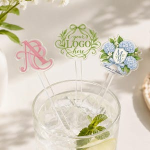 May include: Three clear acrylic drink stirrers in a glass of ice water. One features a pink monogram, one has a green wreath design with the text "your LOGO here", and one displays a blue hydrangea floral crest with "MW" and "Madison & William".