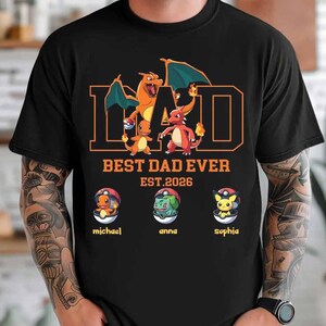 Może przedstawiać: Czarna koszulka z napisem DAD dużymi pomarańczowymi literami oraz grafiką Charizarda i Charmandera. Poniżej znajduje się tekst BEST DAD EVER EST. 2026. Trzy Poké Balle zawierają Charmandera, Bulbasaura i Pikachu z imionami michael, anna oraz sophia.
