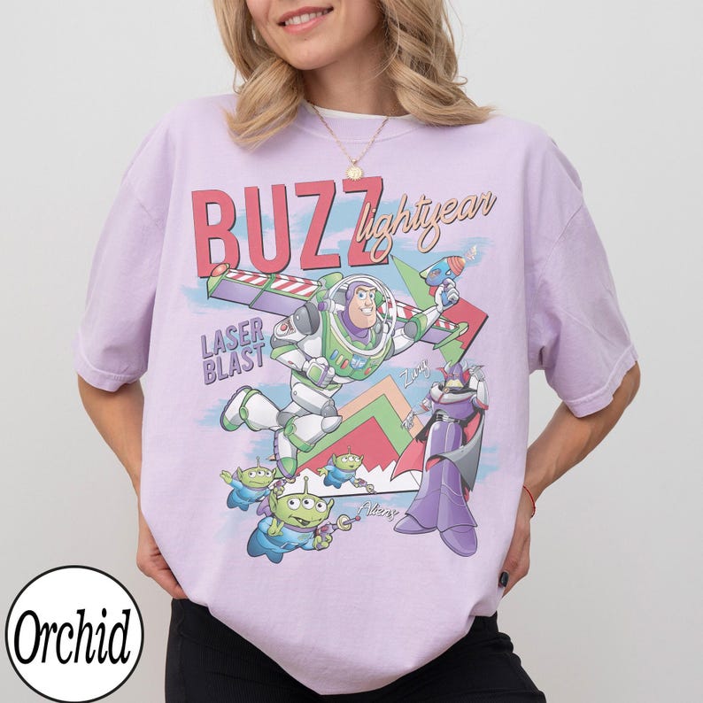 Puede incluir: Una camiseta de color lila claro con un gr&aacute;fico de Buzz Lightyear de Toy Story. El dise&ntilde;o incluye las palabras "BUZZ Lightyear" y "LASER BLAST", junto con personajes de dibujos animados. La camiseta tiene mangas cortas y cuello redondo.