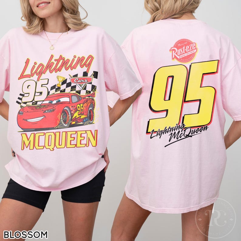 May include: Light pink t-shirt featuring Lightning McQueen from the Cars movie. The front graphic shows McQueen with the number 95, a checkered flag, and the text "Lightning McQueen". The back displays a large yellow "95" and the text "Lightning McQueen".