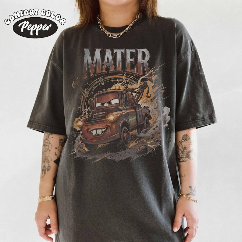 May include: Dark gray t-shirt featuring a graphic of Mater from the movie Cars. The word "MATER" is printed above the image of the character. The shirt also has the words "Comfort Color Pepper" printed on the top left.