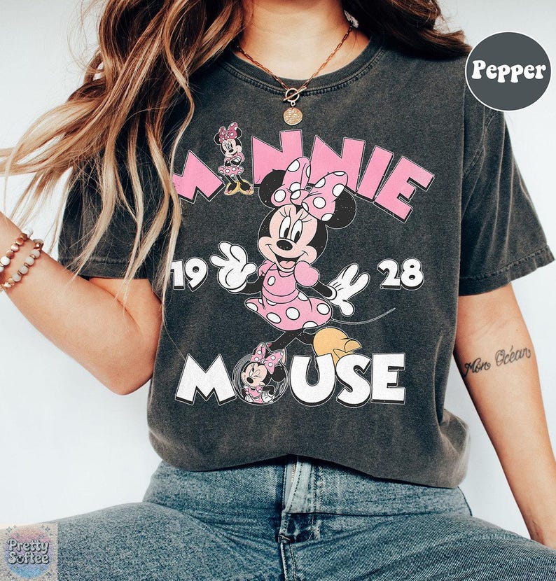 May include: Dark gray t-shirt featuring a Minnie Mouse graphic. The design includes the word "MINNIE" in pink, the year "1928", and the word "MOUSE" in white. Minnie Mouse is depicted in a pink polka dot dress.