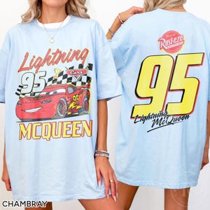 May include: Light blue t-shirt featuring a graphic of Lightning McQueen from the Cars movie. The front design includes the text "Lightning 95 McQueen" with a checkered flag and a red race car. The back displays a large yellow "95" and "Lightning McQueen".
