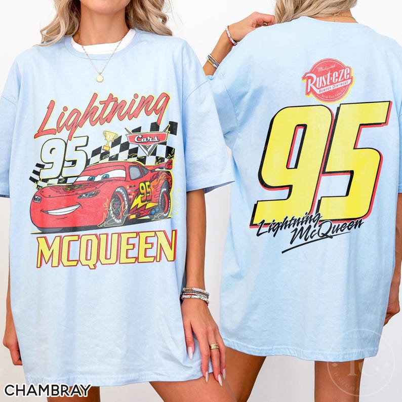 May include: Light blue t-shirt featuring a graphic of Lightning McQueen from the Cars movie. The front design includes the text "Lightning 95 McQueen" with a checkered flag and a red race car. The back displays a large yellow "95" and "Lightning McQueen".