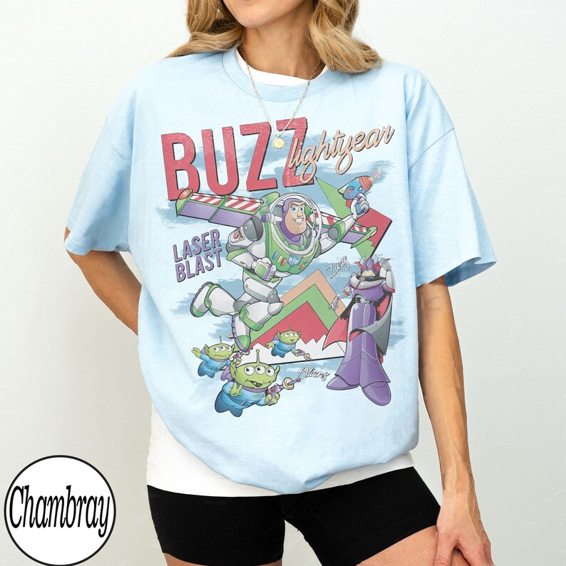 Puede incluir: Camiseta azul claro con un estampado gr&aacute;fico de Buzz Lightyear de Toy Story. El dise&ntilde;o incluye el texto "BUZZ lightyear" y "LASER BLAST", junto con im&aacute;genes de extraterrestres y Zurg. Es una prenda informal.