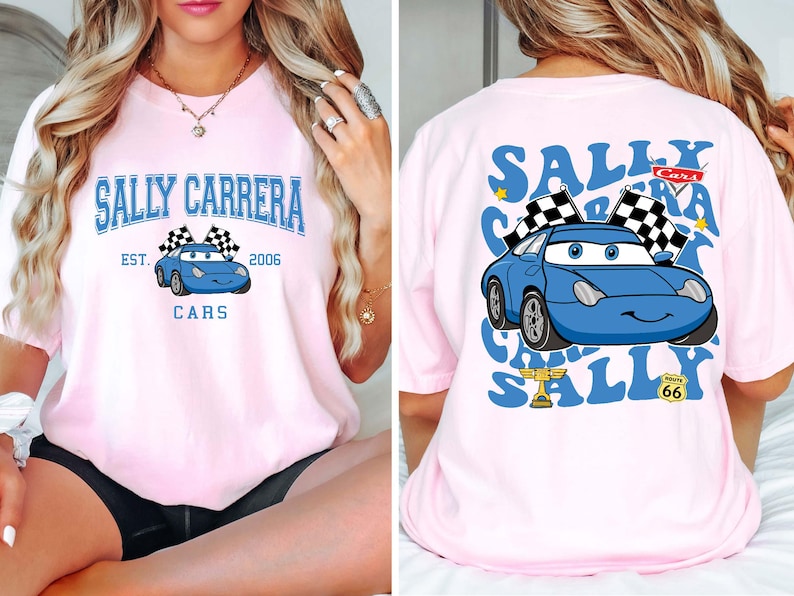 以下が含まれることがあります： 水色のカートゥーンカーのデザインが施された、薄いピンク色のTシャツ。「SALLY CARRERA」と「CARS」の文字が前面にプリントされ、「EST. 2006」の文字も。背面には車、チェッカーフラッグ、そして「SALLY CARRERA」の文字が繰り返されています。