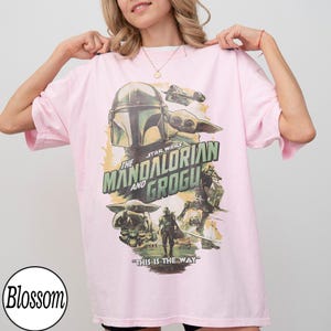 K&ouml;nnte beinhalten: Hellrosa T-Shirt mit einem Star Wars-Design mit The Mandalorian und Grogu. Die Grafik zeigt einen Helm, Grogu und den Satz "This is the Way" in gr&uuml;n-wei&szlig;er Schrift.