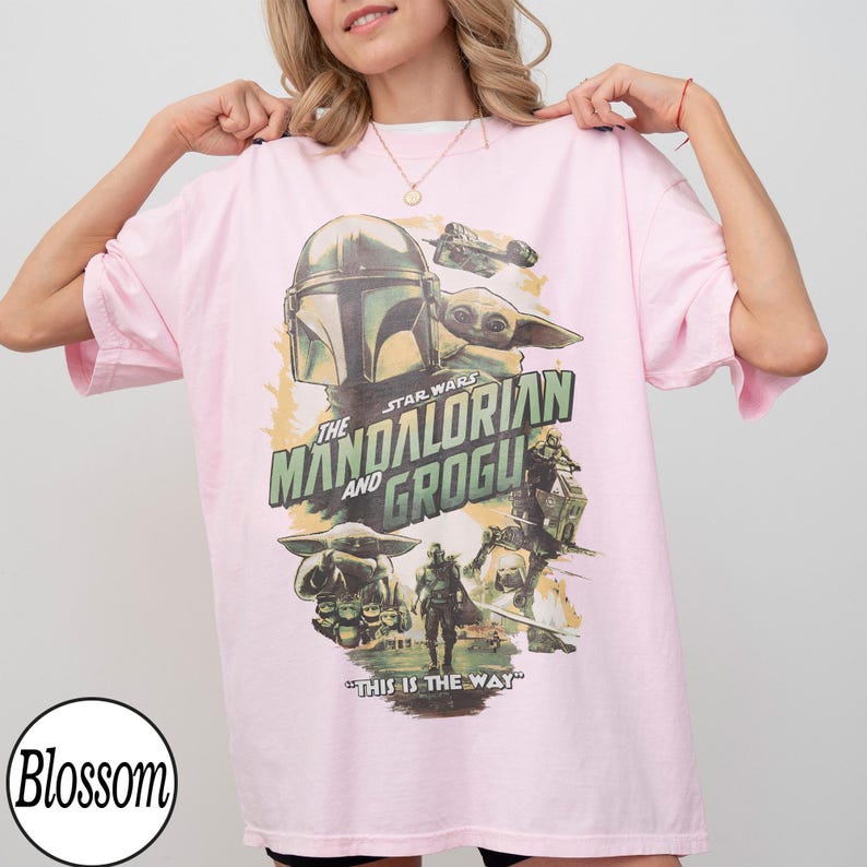 K&ouml;nnte beinhalten: Hellrosa T-Shirt mit einem Star Wars-Design mit The Mandalorian und Grogu. Die Grafik zeigt einen Helm, Grogu und den Satz "This is the Way" in gr&uuml;n-wei&szlig;er Schrift.