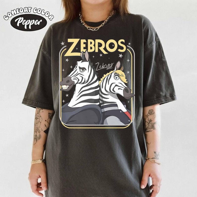 May include: Dark gray t-shirt featuring a cartoon graphic of two zebras with the word "ZEBROS" in yellow. The shirt has a vintage, worn look, with the Comfort Colors and Pepper logos in the upper left corner.