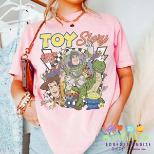 K&ouml;nnte beinhalten: Rosa T-Shirt mit einer Toy Story-Grafik mit Woody, Buzz Lightyear, Rex und den kleinen gr&uuml;nen M&auml;nnchen. Das Shirt zeigt die Worte "TOY STORY" und "SINCE 1995".