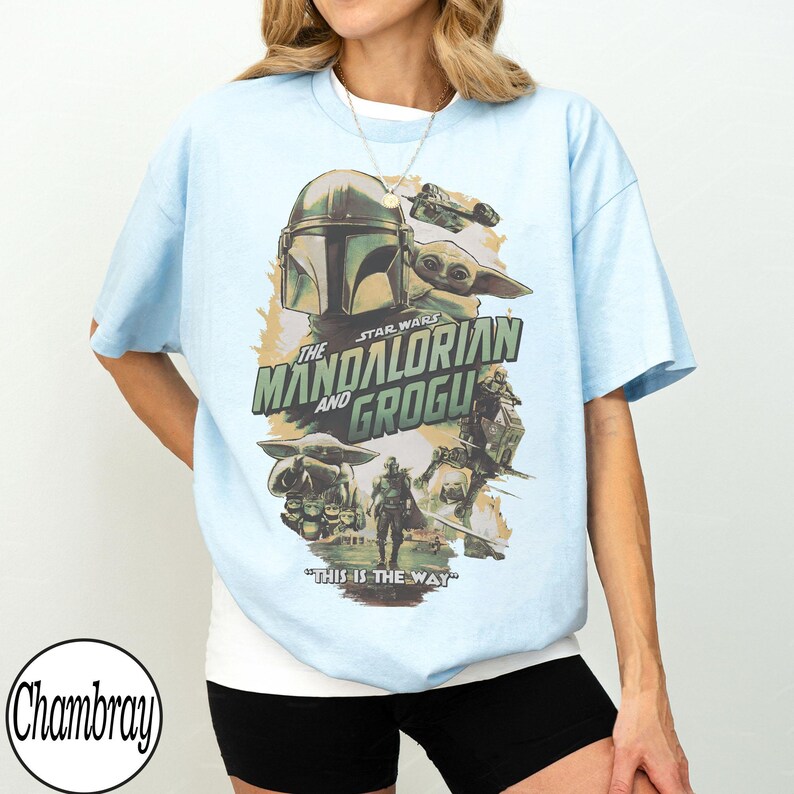 K&ouml;nnte beinhalten: Hellblaues T-Shirt mit einem Star Wars-Motiv von The Mandalorian und Grogu. Das Design zeigt den Helm des Mandalorianers, Grogu und den Schriftzug "THIS IS THE WAY".