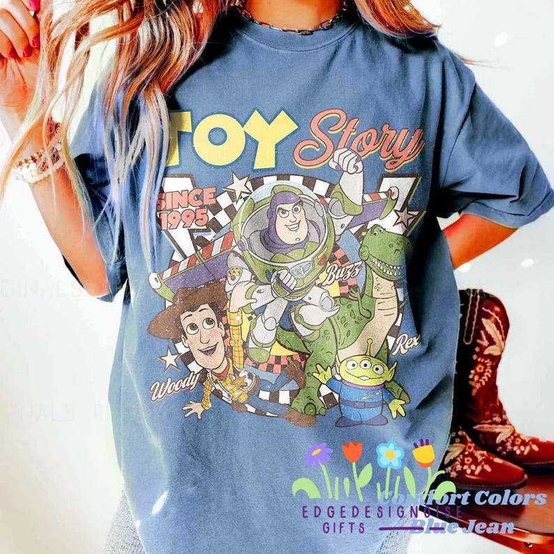 K&ouml;nnte beinhalten: Blaues T-Shirt mit einem Grafikdruck von Figuren aus dem Film "Toy Story". Das Design umfasst Buzz Lightyear, Woody, Rex und die kleinen gr&uuml;nen M&auml;nnchen, mit dem Text "Toy Story Since 1995."