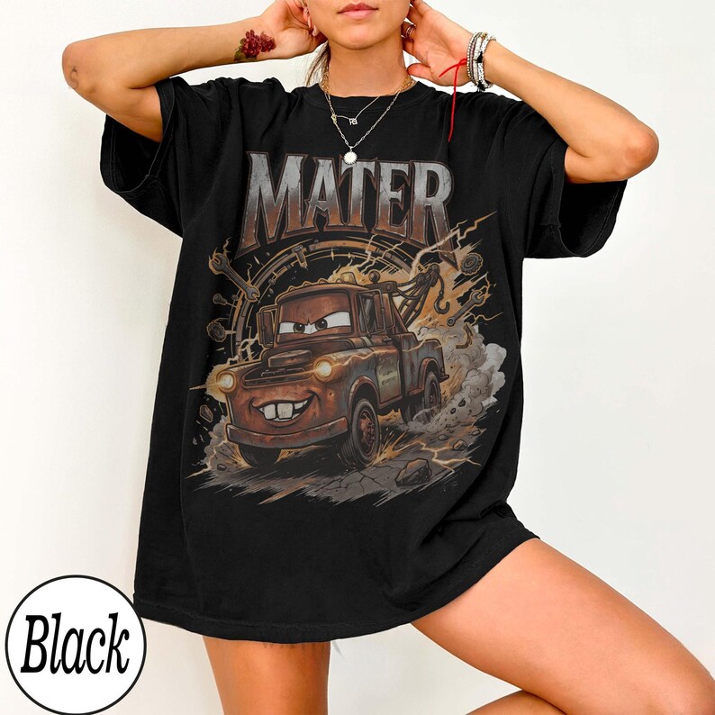 May include: Black t-shirt featuring a graphic of Mater from the movie Cars. The design includes the word "MATER" in a distressed font above an illustration of the character. The image shows Mater driving with a background of tools and lightning.