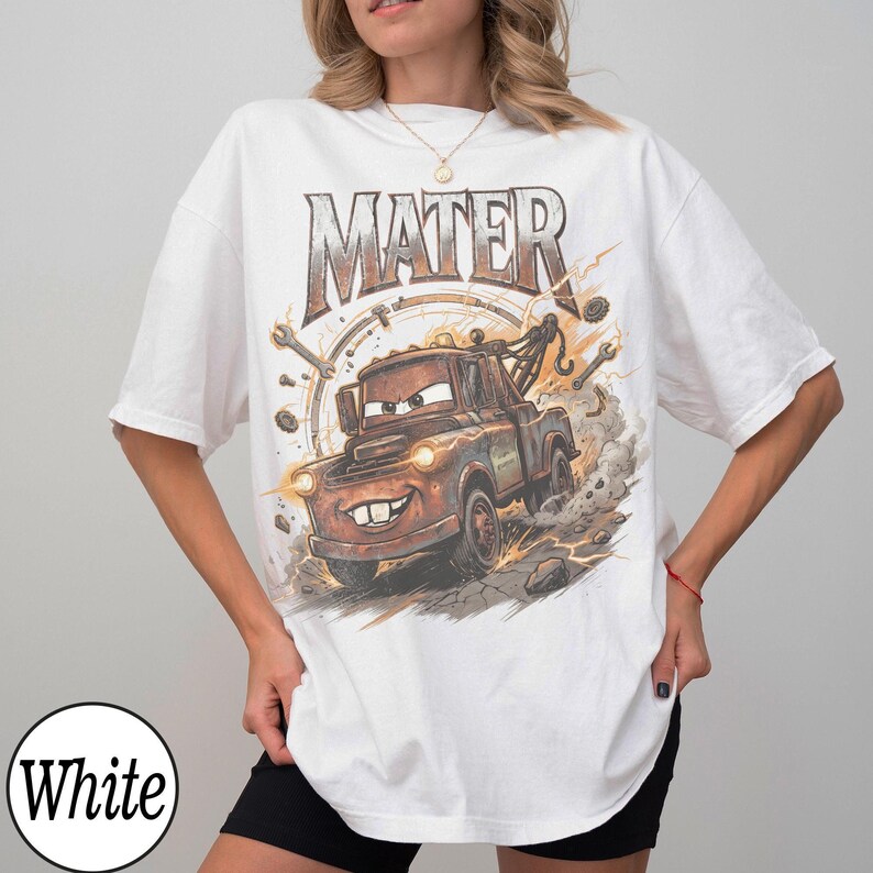 May include: White t-shirt featuring a graphic of Mater from the movie Cars. The design includes the word "MATER" in large letters above the character, with a background of tools and a clock. The cartoon tow truck is brown and has a smiling face.