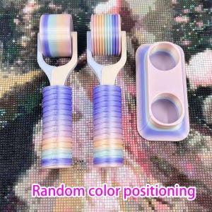May include: Two roller tools and a pink and purple holder for diamond painting. The rollers have a rainbow gradient design, with purple handles. The text "Random color positioning" is at the bottom of the image.