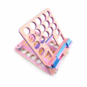 May include: A pink and blue wooden organizer with multiple circular holes. The organizer has a hinged design, allowing it to fold flat. The color scheme includes pink, blue, and yellow accents, creating a visually appealing aesthetic.