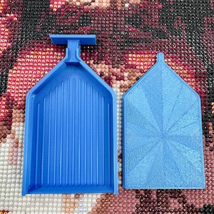 May include: Two blue plastic diamond painting trays. One tray has a handle and vertical grooves, the other has a textured starburst pattern. The trays are designed to hold and organize small craft items.