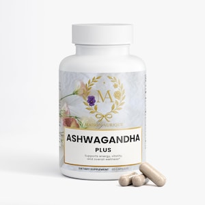 May include: A white supplement bottle with a gold label featuring the text "ASHWAGANDHA PLUS". The label also includes the text "Supports energy, vitality, and overall wellness". Several beige capsules are in front of the bottle. The bottle has a white cap.