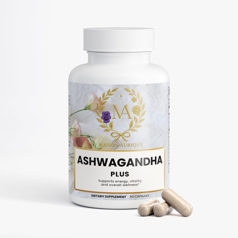 May include: A white supplement bottle with a gold label featuring the text "ASHWAGANDHA PLUS". The label also includes the text "Supports energy, vitality, and overall wellness". Several beige capsules are in front of the bottle. The bottle has a white cap.