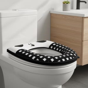 以下が含まれることがあります： 白のトイレと、白と黒のパンダをテーマにした便座カバー。 シートカバーは黒い縁取りと、黒い正方形と白いひし形のパターンがあります。 パンダの顔はシートの前面にあります。