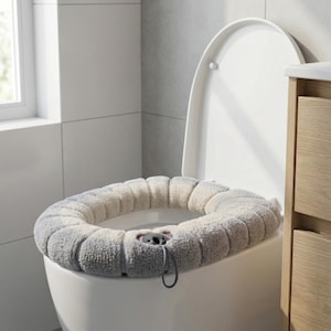 Könnte beinhalten: Ein weicher, grau-weißer Toilettensitzbezug mit Koala-Bär-Design. Der Bezug besteht aus einem weichen, strukturierten Material und hat einen Kordelzugverschluss. Der Toilettensitz ist weiß, in einem Badezimmer.