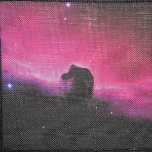 Puede incluir: Una imagen en blanco y negro de una nebulosa con una silueta oscura en forma de cabeza de caballo en el centro. La nebulosa es de color rosa brillante con algunas estrellas blancas dispersas.