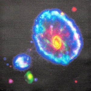 Puede incluir: Un fondo de tela negro con un diseño de nebulosa colorido. La nebulosa es de un azul brillante con un centro amarillo y acentos rosados y morados. Hay orbes más pequeños y brillantes dispersos alrededor de la nebulosa.