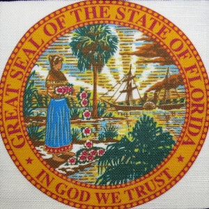 May include: The Great Seal of the State of Florida depicts a woman in a blue dress holding a bunch of flowers, a palm tree, a steamboat, and the words "In God We Trust".