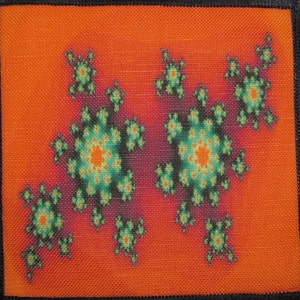 May include: A close-up of a fabric patch with a colorful fractal design. The design features a repeating pattern of green, orange, and yellow shapes on a red background.