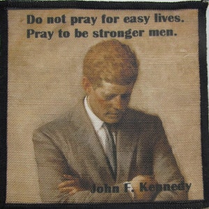 Può includere: Un'immagine in bianco e nero di John F. Kennedy con la citazione "Non pregare per vite facili. Prega per essere uomini più forti." La citazione è stampata su uno sfondo beige.