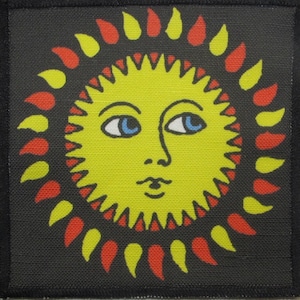 May include: A yellow sun with a face and blue eyes surrounded by red and yellow flames on a black background.