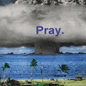 May include: A black and white photo of a mushroom cloud over a body of water. The text "Pray." is written in blue letters on the cloud.