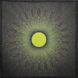 May include: A black and white patch with a yellow circle in the center. The circle is surrounded by concentric circles of black and white lines.