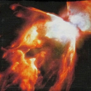 Puede incluir: Un primer plano de una nebulosa naranja y amarilla ardiente con un centro blanco. La nebulosa está sobre un fondo negro.