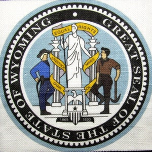 Op de afbeelding: Het Grote Zegel van de staat Wyoming heeft een blauw en wit cirkelvormig ontwerp met de woorden "Great Seal of the State of Wyoming" rond de buitenkant. Het midden van het zegel toont een vrouw die op een voetstuk staat met een houweel en een ploeg, die de industrieën van de staat vertegenwoordigen. De vrouw wordt omringd door twee pilaren met de woorden "Equal Rights" en "Livestock, Grain, Mines" erop gegraveerd. Het zegel bevat ook het jaar 1890.