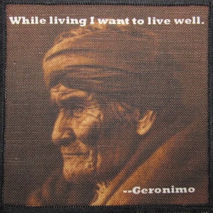 Puede incluir: Parche cuadrado con un retrato en tonos sepia de Gerónimo de perfil. La imagen incluye la cita "While living I want to live well." y el nombre "...Geronimo" en texto blanco. El parche tiene un borde negro.