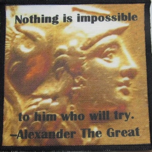 May include: A gold-toned patch with a quote from Alexander the Great. The quote reads "Nothing is impossible to him who will try. -Alexander The Great". The background is a close-up of a person's face.