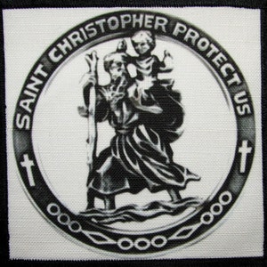 以下が含まれることがあります： 聖クリストファーが子供を抱いている円形のデザインが施された、黒と白の刺繍パッチ。円周には「Saint Christopher Protect Us」という文字が書かれている。