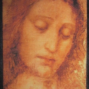 May include: A close-up of a vintage-style printed image of a woman's face. The image is printed on a brown fabric with a textured surface. The woman's eyes are closed and her lips are slightly parted. The image is in a muted brown color palette.