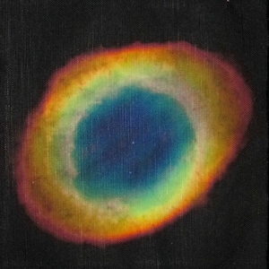 Puede incluir: Primer plano de un patrón circular iridiscente sobre un fondo de tela negro. El patrón es un anillo de colores, incluyendo rojo, naranja, amarillo, verde, azul y morado, con un centro azul oscuro.