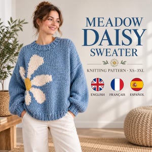 Op de afbeelding: Een grof gebreide blauwe trui met een grote witte madeliefjesafbeelding met een geel hart. De tekst luidt MEADOW DAISY SWEATER KNITTING PATTERN XS-3XL. Drie ronde iconen tonen de vlaggen van het Verenigd Koninkrijk, Frankrijk en Spanje met labels.