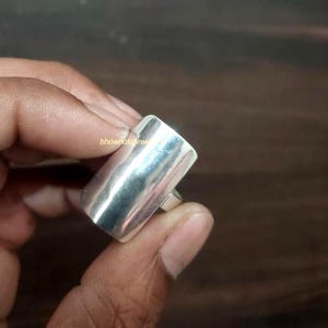 May include: A silver-colored ring with a rectangular design. The ring has a smooth, polished surface and a simple, modern aesthetic. The ring is shown in a close-up shot.
