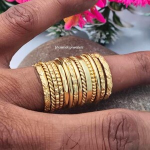 May include: A stack of ten gold rings worn on a finger, featuring various textures including twisted rope patterns, smooth polished bands, and engraved designs. The text bhawnakjewellers is visible in the center of the image above the rings.