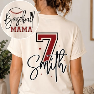 K&ouml;nnte beinhalten: Ein cremefarbenes T-Shirt mit einer gro&szlig;en kastanienbraunen Nummer 7 und dem Namen Smith in schwarzer Schreibschrift. Ein kreisf&ouml;rmiger Einsatz zeigt den Text Baseball MAMA in Schwarz und Kastanienbraun mit Baseball-Grafik und Punkten.