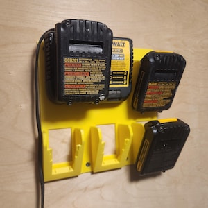 May include: A yellow battery organizer with three slots, holding three black battery packs. The organizer is mounted on a wooden surface. The battery packs have warning labels and model numbers.